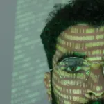 Mann mit projiziertem Binärcode im Gesicht als Symbol für KI-manipulierte Medien
