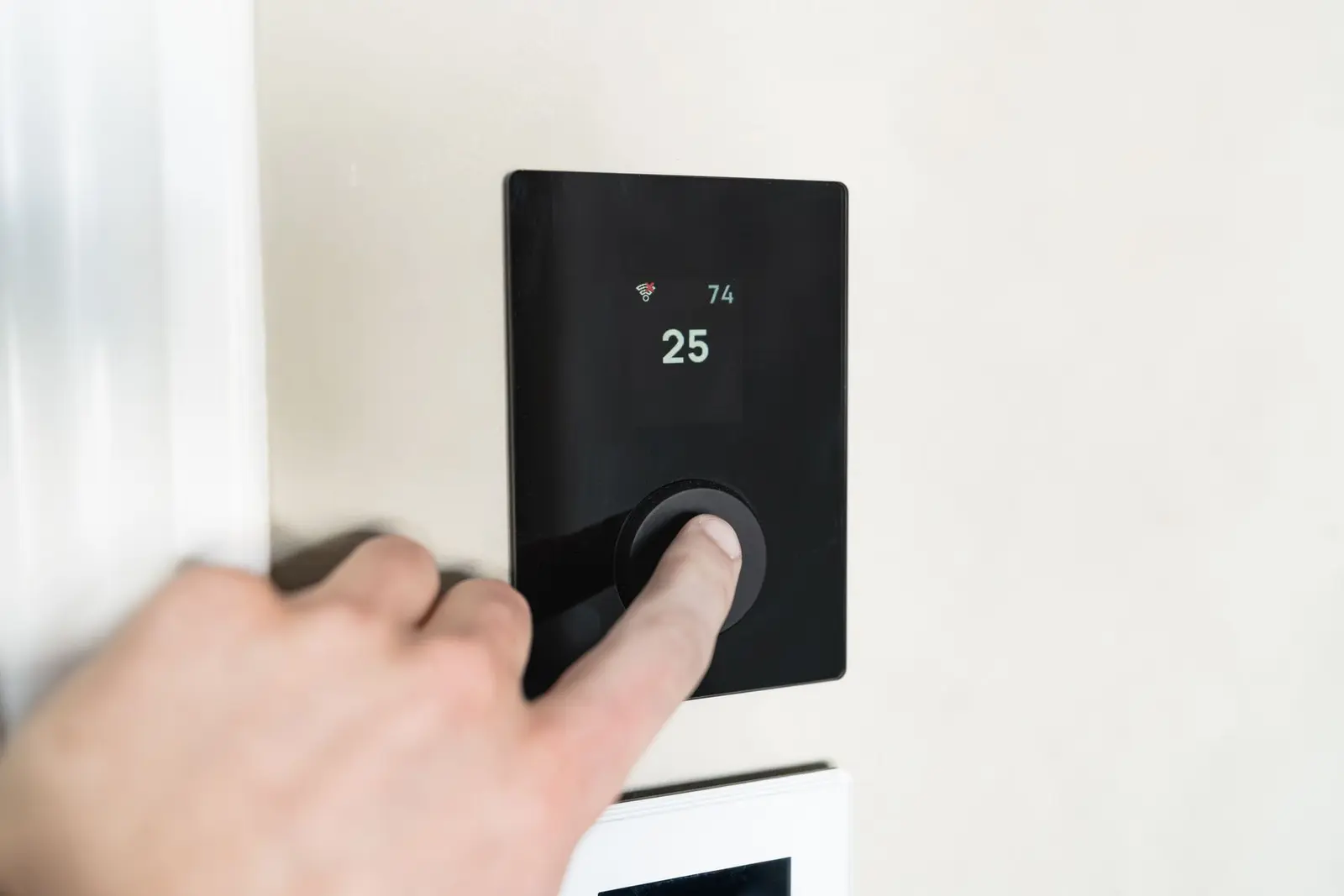 Hand stellt ein digitales Wandthermostat mit Temperaturanzeige ein