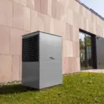 Außengerät einer Wärmepumpe vor der Fassade eines modernen Wohnhauses