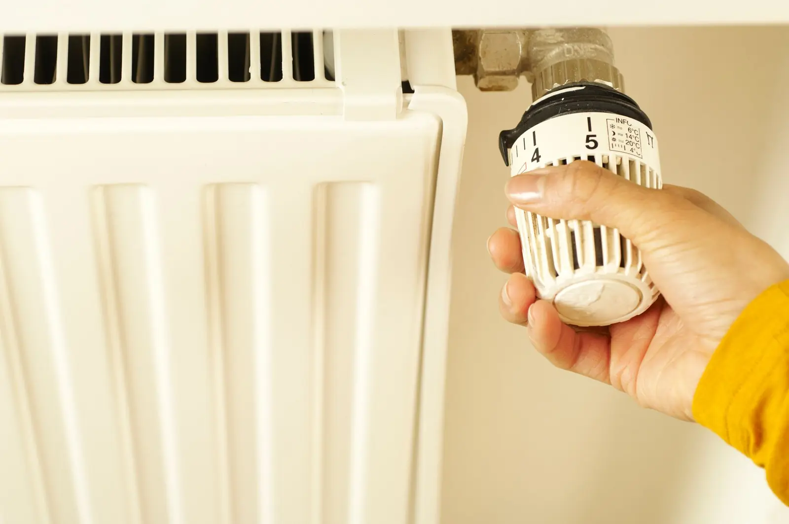Hand stellt den Thermostatknopf an einem weißen Heizkörper ein