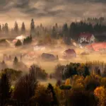 Herbstliches Dorf liegt am Morgen unter einer flachen Nebeldecke