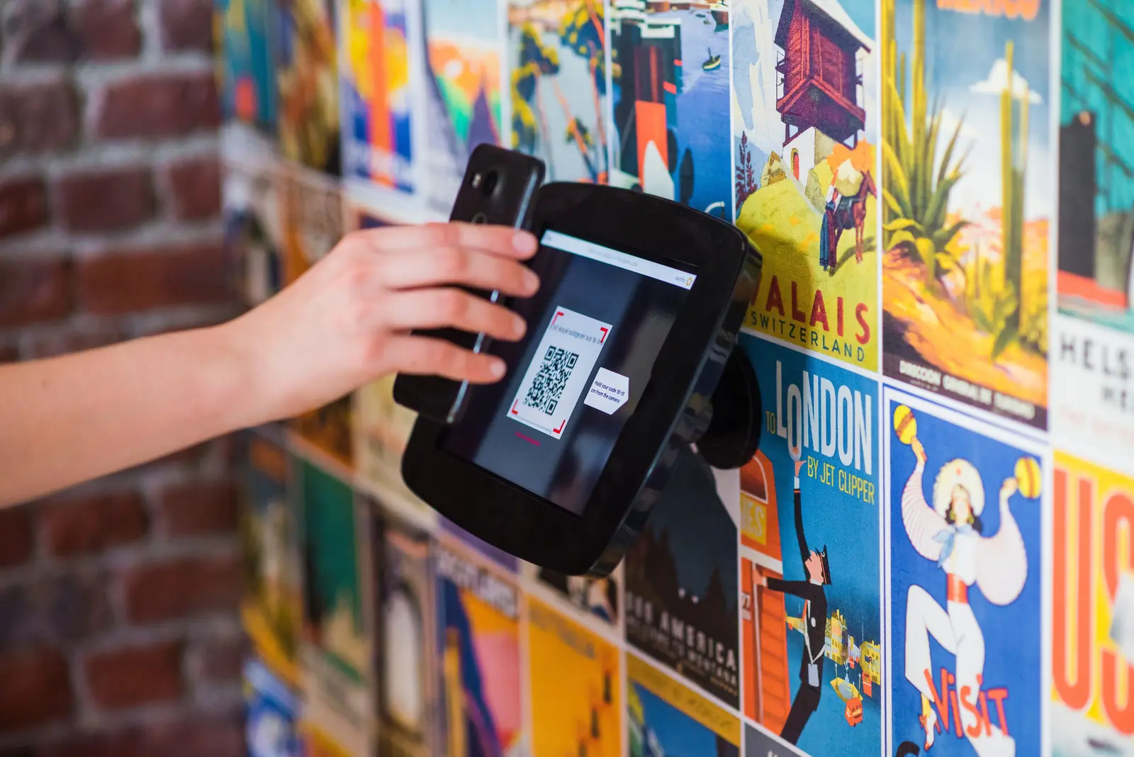 Eine Person hält ein Smartphone vor einen QR-Code an einem öffentlich zugänglichen Terminal