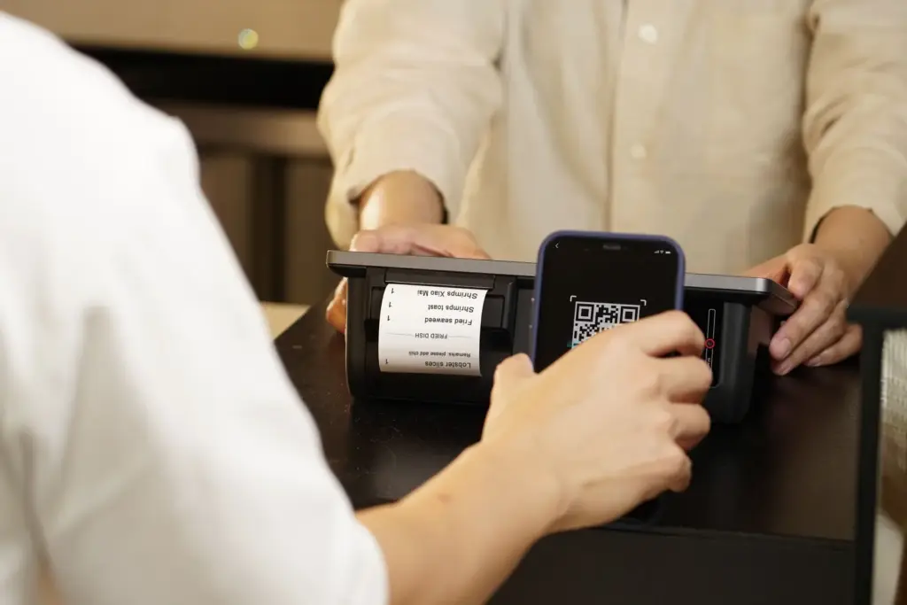 Eine Person scannt mit dem Smartphone einen QR-Code an einem Zahlungsterminal