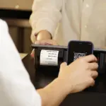 Eine Person scannt mit dem Smartphone einen QR-Code an einem Zahlungsterminal