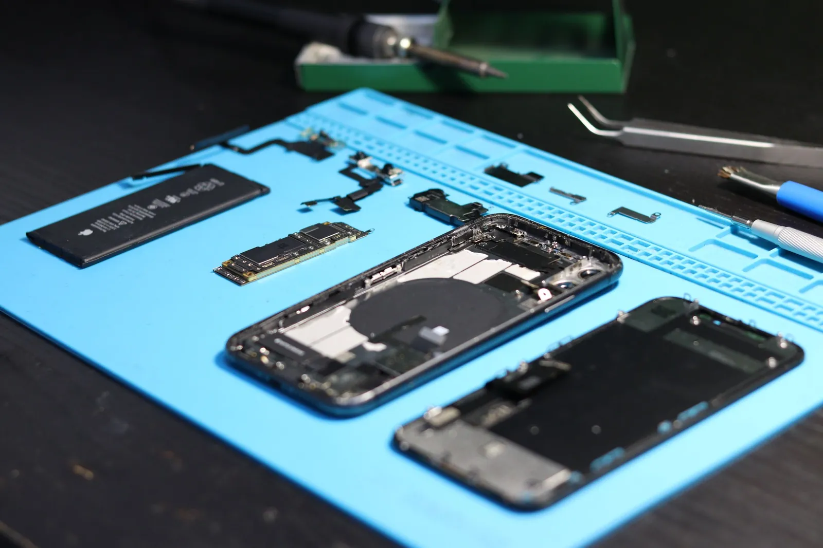 Zerlegtes Smartphone mit Akku, Platine und Werkzeugen auf einer Reparaturmatte