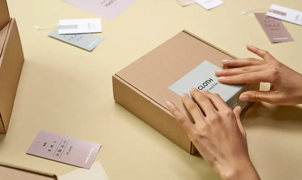 Hände bringen ein Etikett auf einer schlichten Produktverpackung an