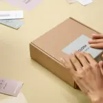 Hände bringen ein Etikett auf einer schlichten Produktverpackung an