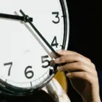 Hand stellt die Zeiger einer großen Analoguhr für die Zeitumstellung ein