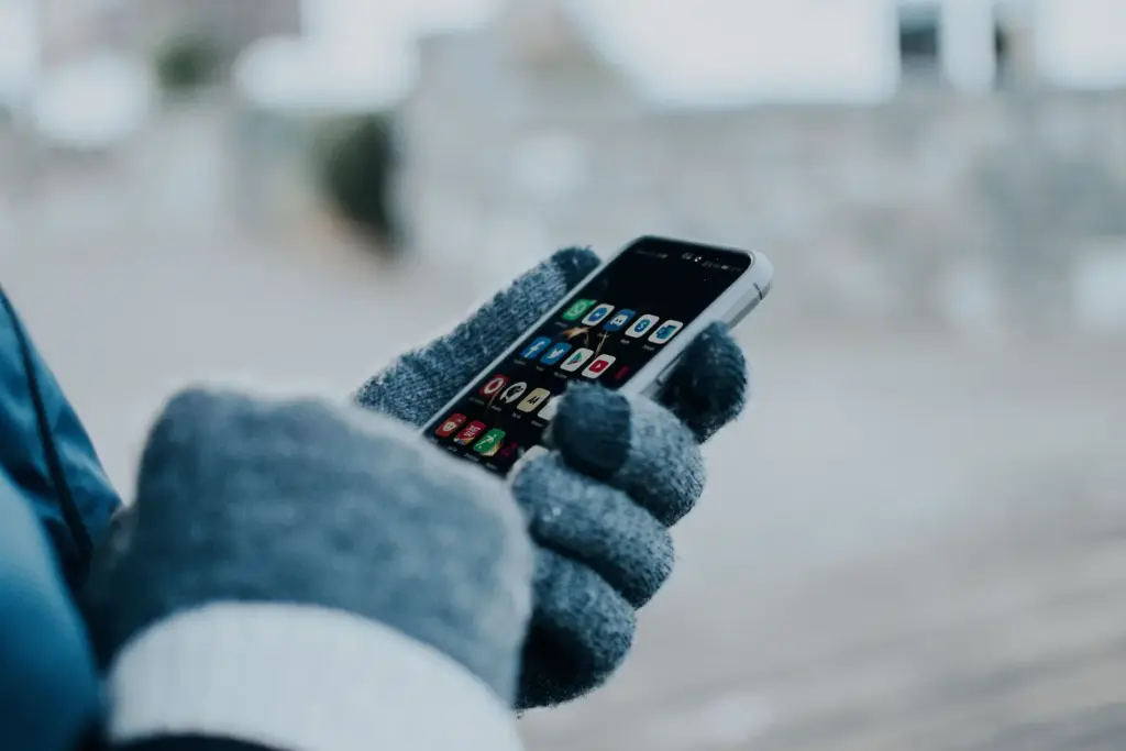 Person bedient ein Smartphone mit dicken Winterhandschuhen im Freien
