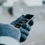 Person bedient ein Smartphone mit dicken Winterhandschuhen im Freien
