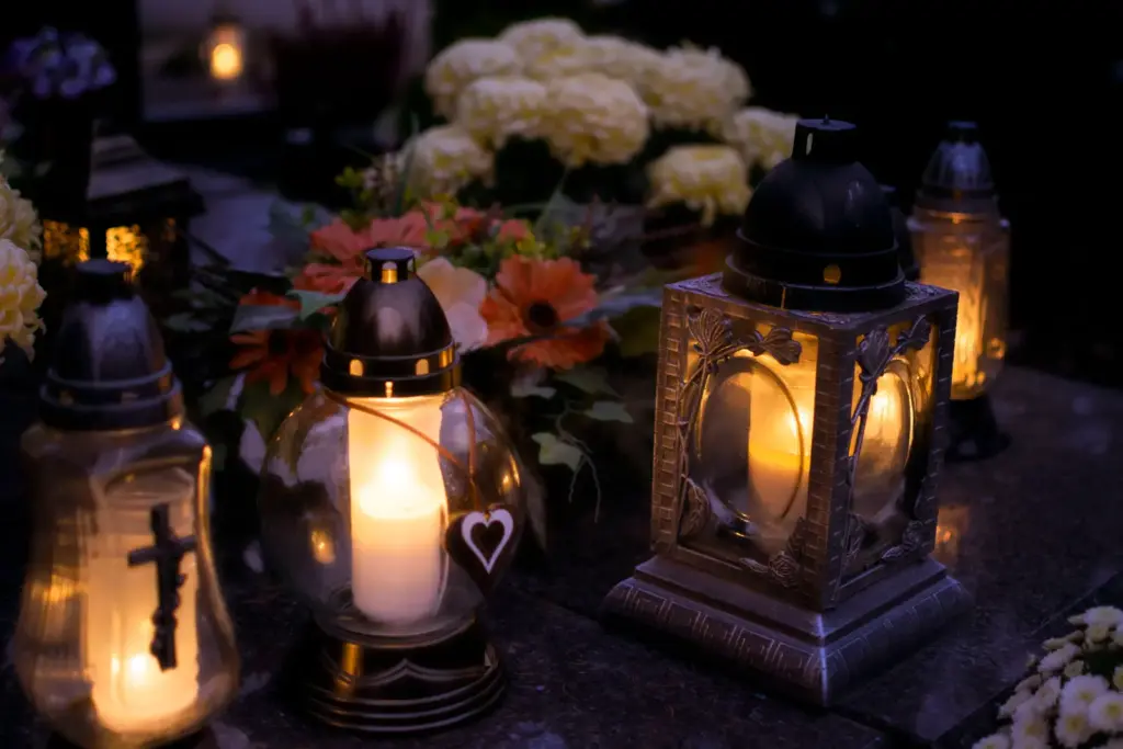 Leuchtende Grablichter und Blumen auf einem Friedhof an Allerheiligen