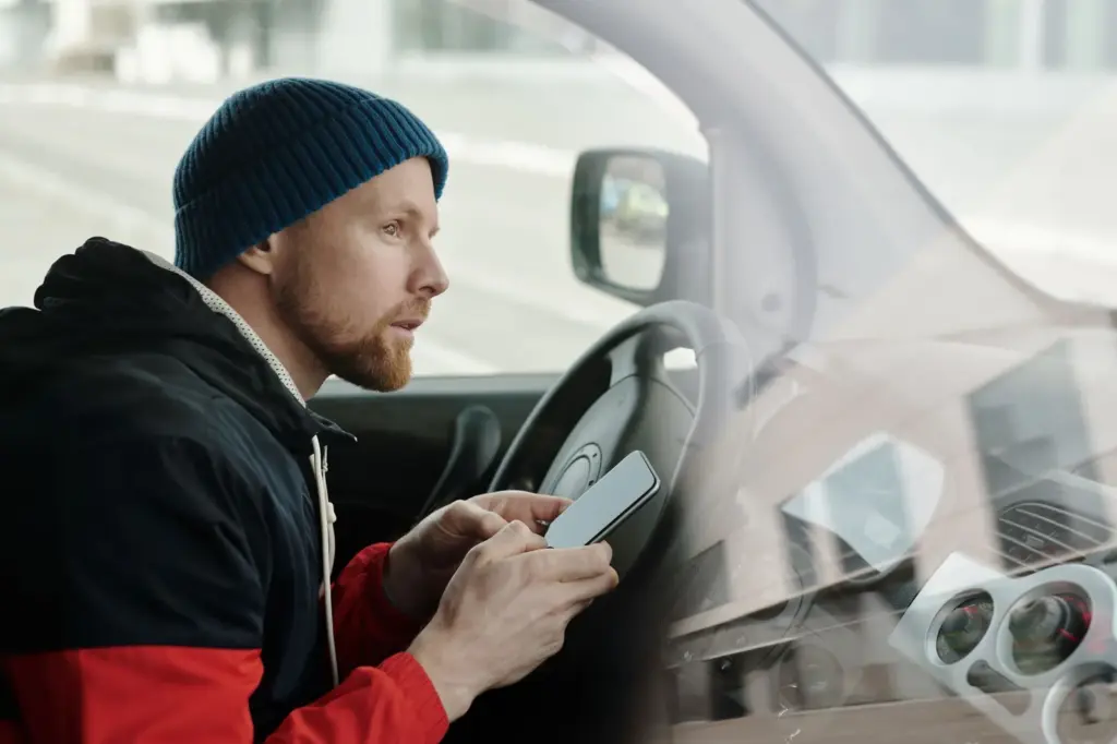 Mann nutzt ein Smartphone in einem geparkten Auto als Symbol für den digitalen Fahrzeugschein