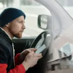 Mann nutzt ein Smartphone in einem geparkten Auto als Symbol für den digitalen Fahrzeugschein