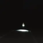 Radfahrer mit eingeschaltetem weißen Frontlicht auf dunkler Straße bei Nacht