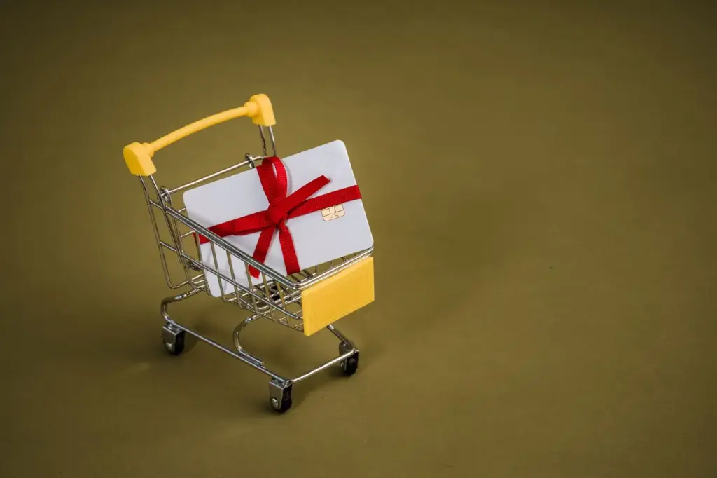 Geschenkgutschein mit roter Schleife in einem kleinen Einkaufswagen