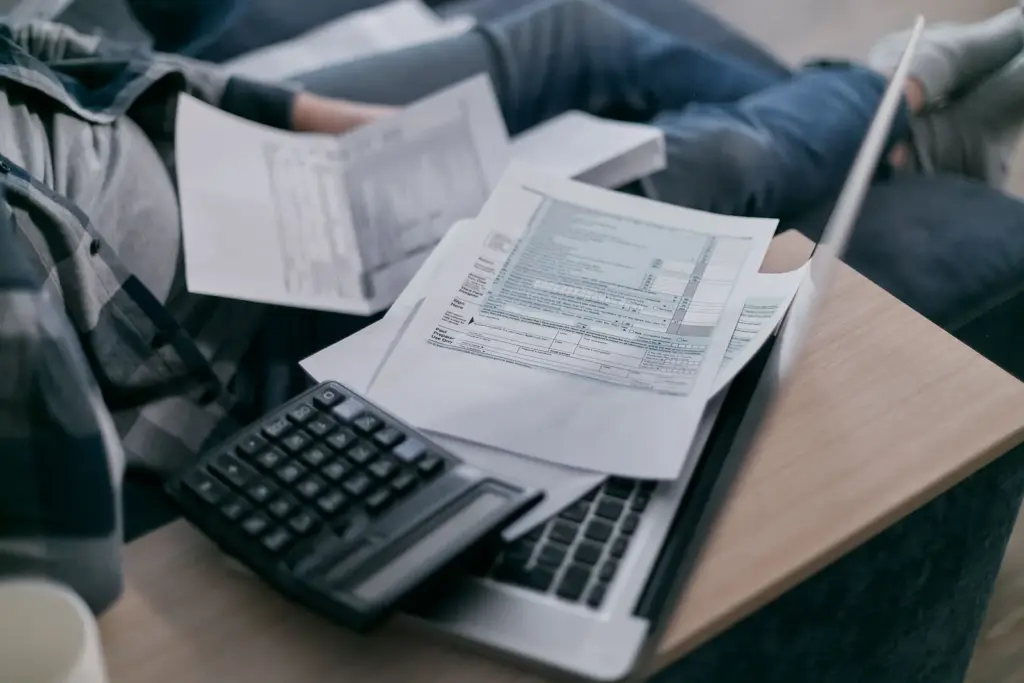 Person prüft Abrechnungsunterlagen mit Taschenrechner auf einem Laptop