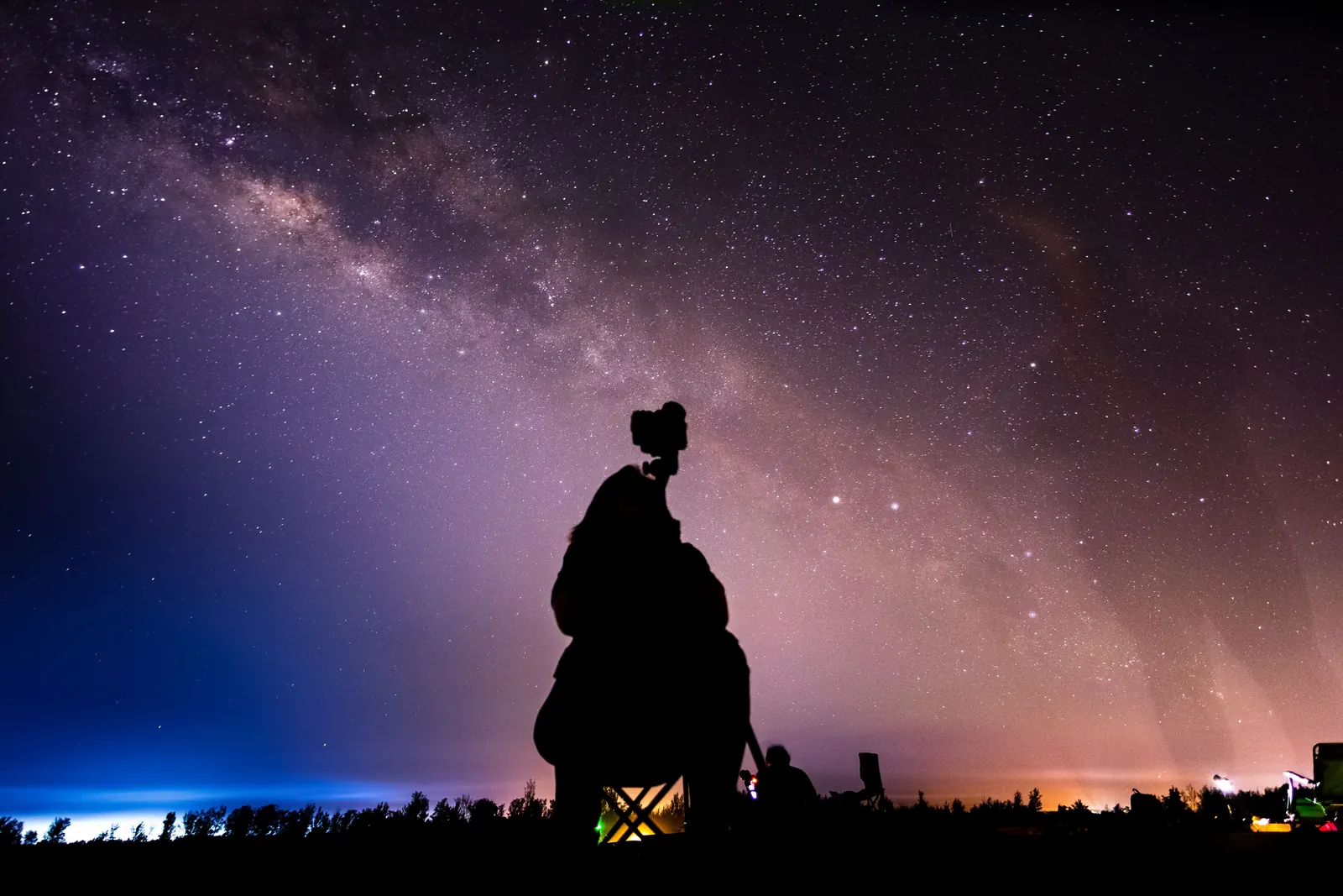 Sitzende Person fotografiert mit einer Kamera den dunklen Sternenhimmel