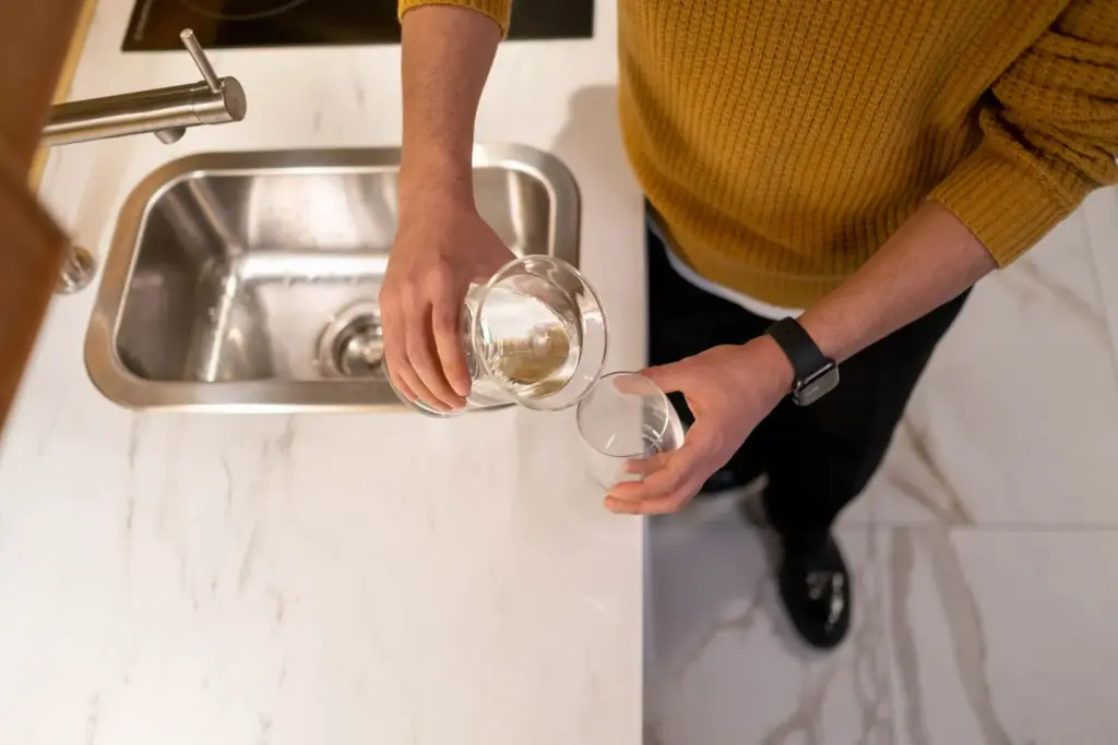 Eine Person gießt in einer Küche Trinkwasser in ein Glas
