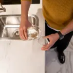 Eine Person gießt in einer Küche Trinkwasser in ein Glas