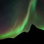 Grüne Polarlichter über einer dunklen Bergsilhouette und Sternenhimmel