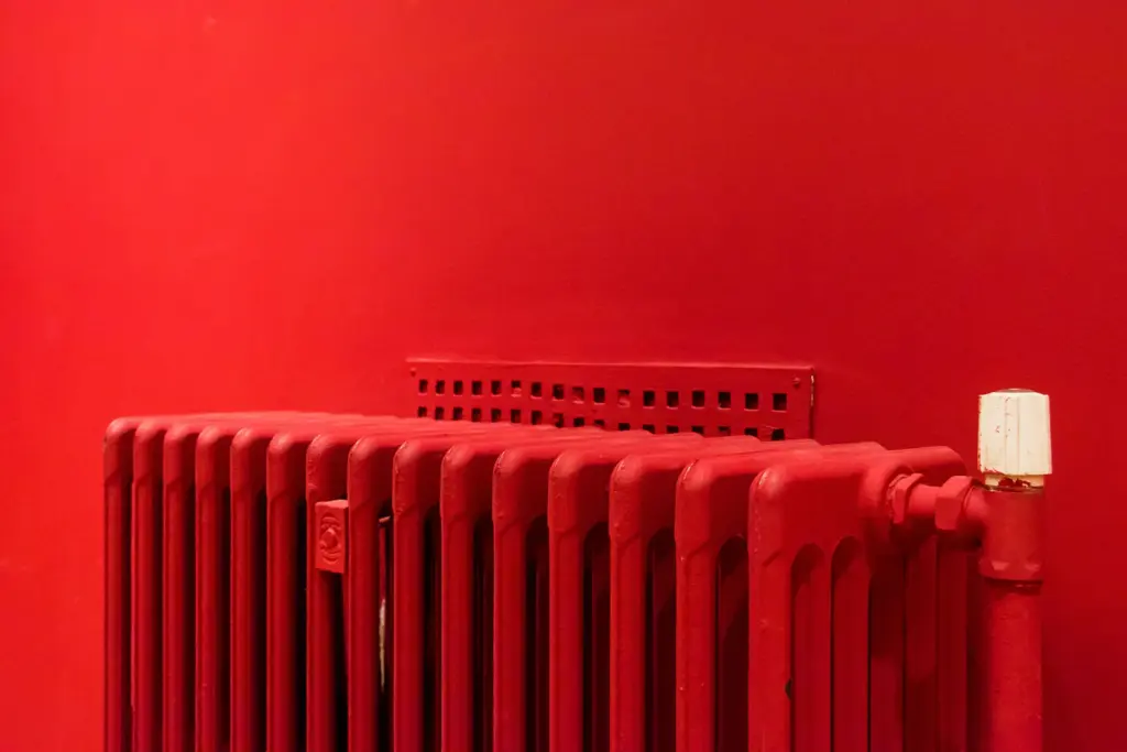 Roter Rippenheizkörper vor einer roten Wand mit weißem Thermostat