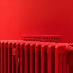 Roter Rippenheizkörper vor einer roten Wand mit weißem Thermostat