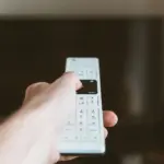 Hand mit Fernbedienung vor einem Fernseher als Symbol für vernetzte TV-Geräte