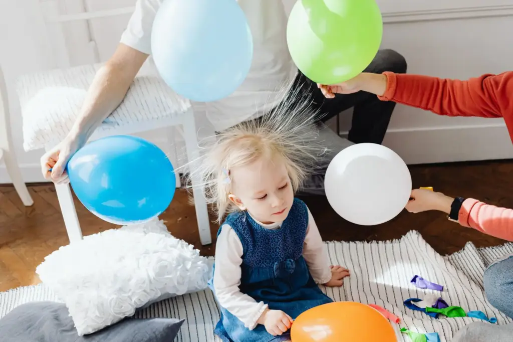 Kind mit durch statische Aufladung abstehenden Haaren zwischen Luftballons