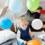Kind mit durch statische Aufladung abstehenden Haaren zwischen Luftballons