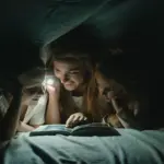 Mutter und zwei Kinder lesen im dunklen Raum bei Taschenlampenlicht
