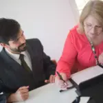 Ältere Frau unterzeichnet Vorsorgedokumente im Beisein eines Beraters
