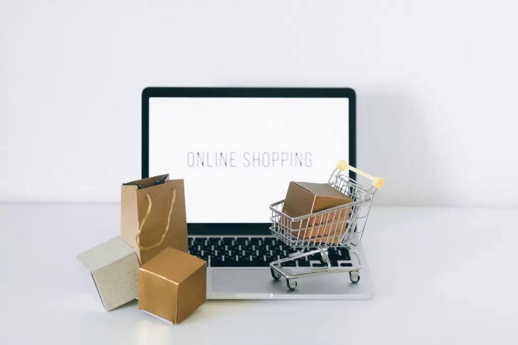 Laptop mit Online-Shop sowie Pakete und kleiner Einkaufswagen auf einem Tisch