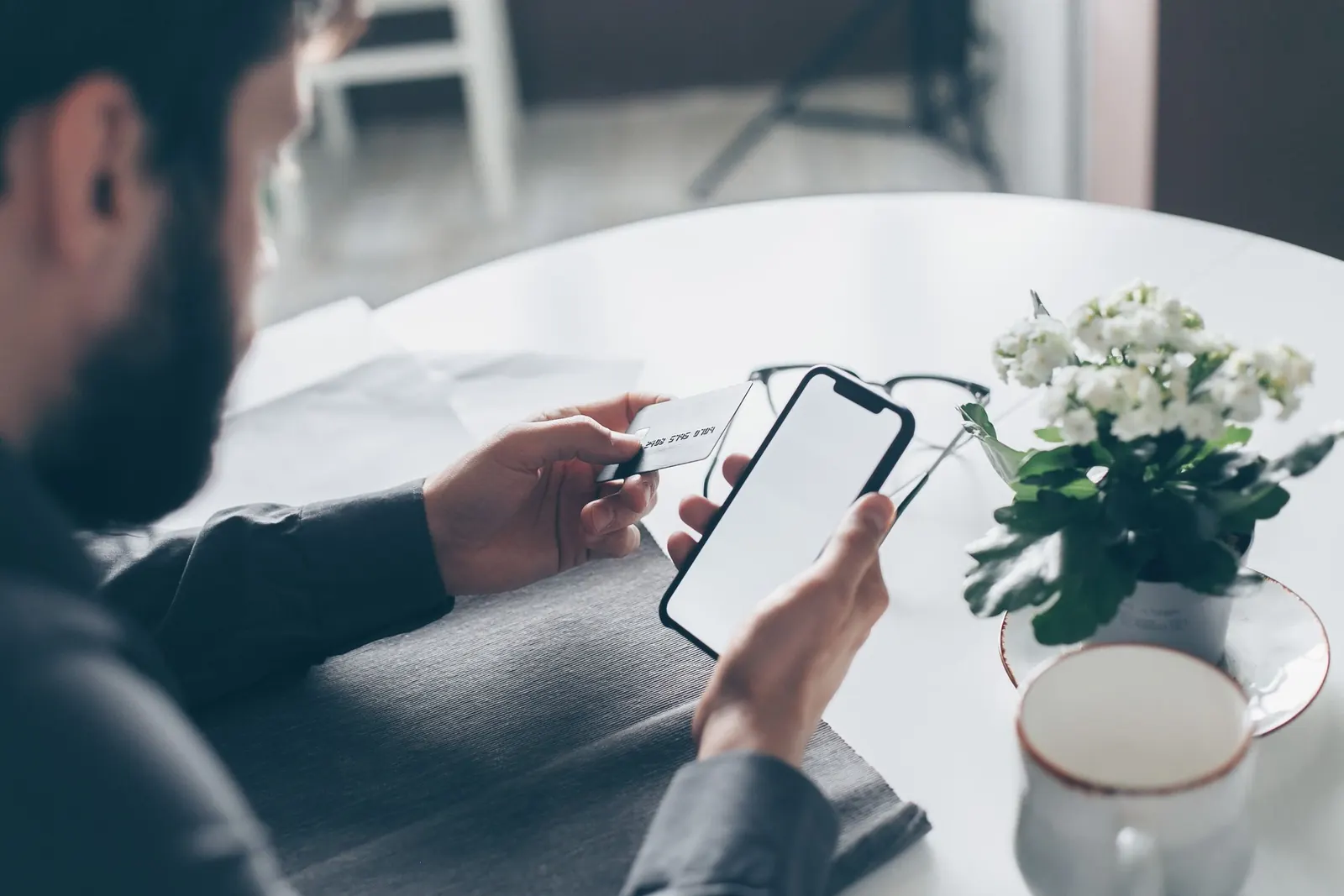 Mann hält beim mobilen Bezahlen eine Kreditkarte und ein Smartphone in den Händen